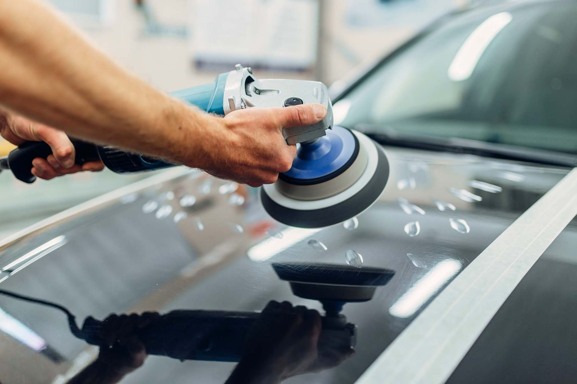 Un homme polit le capot d'une voiture avec une machine.