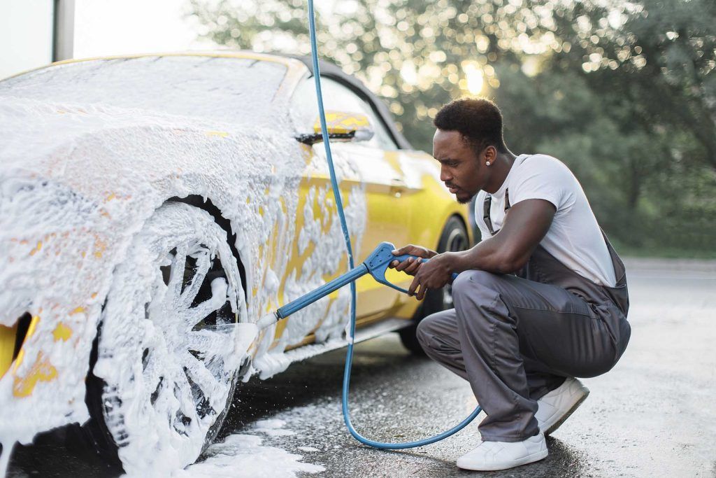 Un homme s'agenouille pour laver une voiture jaune avec de la mousse.