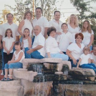 Large family posing on stone steps by a waterfall, all dressed in white and blue.