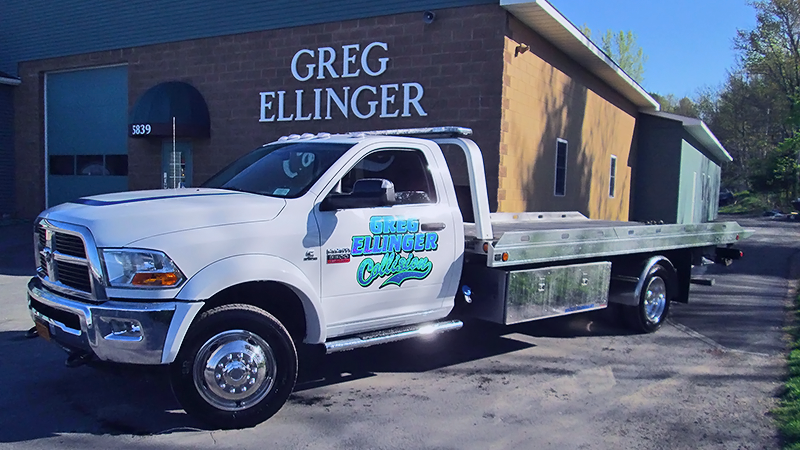 White flatbed truck parked outside Greg Ellinger building, with company logo on the door.