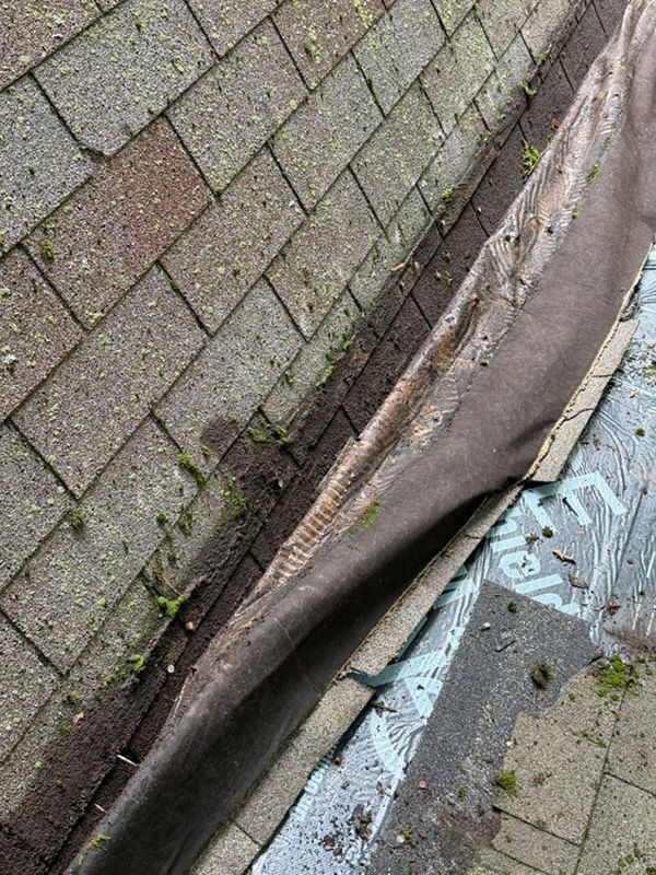 Damaged curbside pavement with a lifted edge beside brick pavers and a cracked concrete drain area