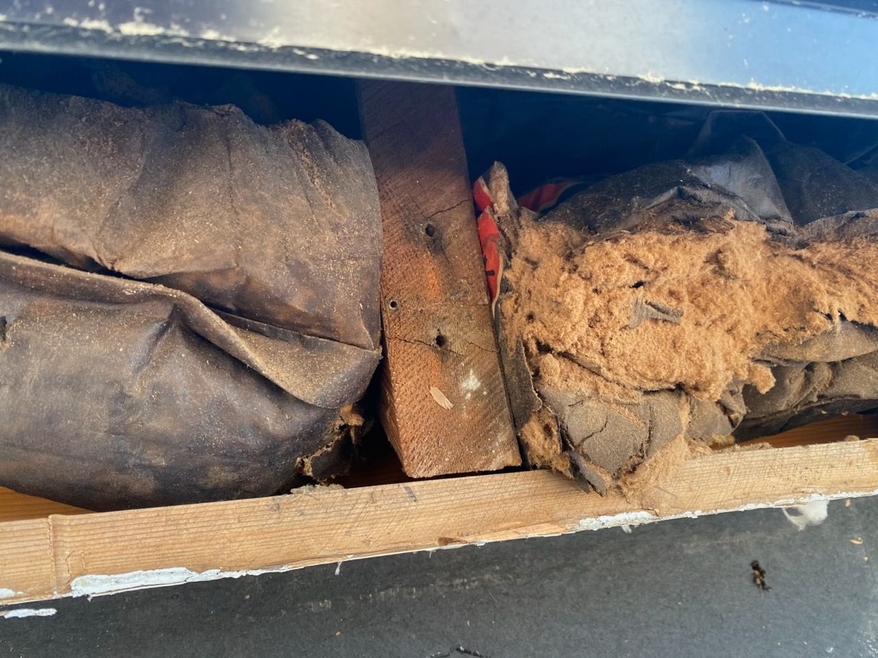 Damaged wall cavity with torn insulation, exposed wood, and a rusted metal strap