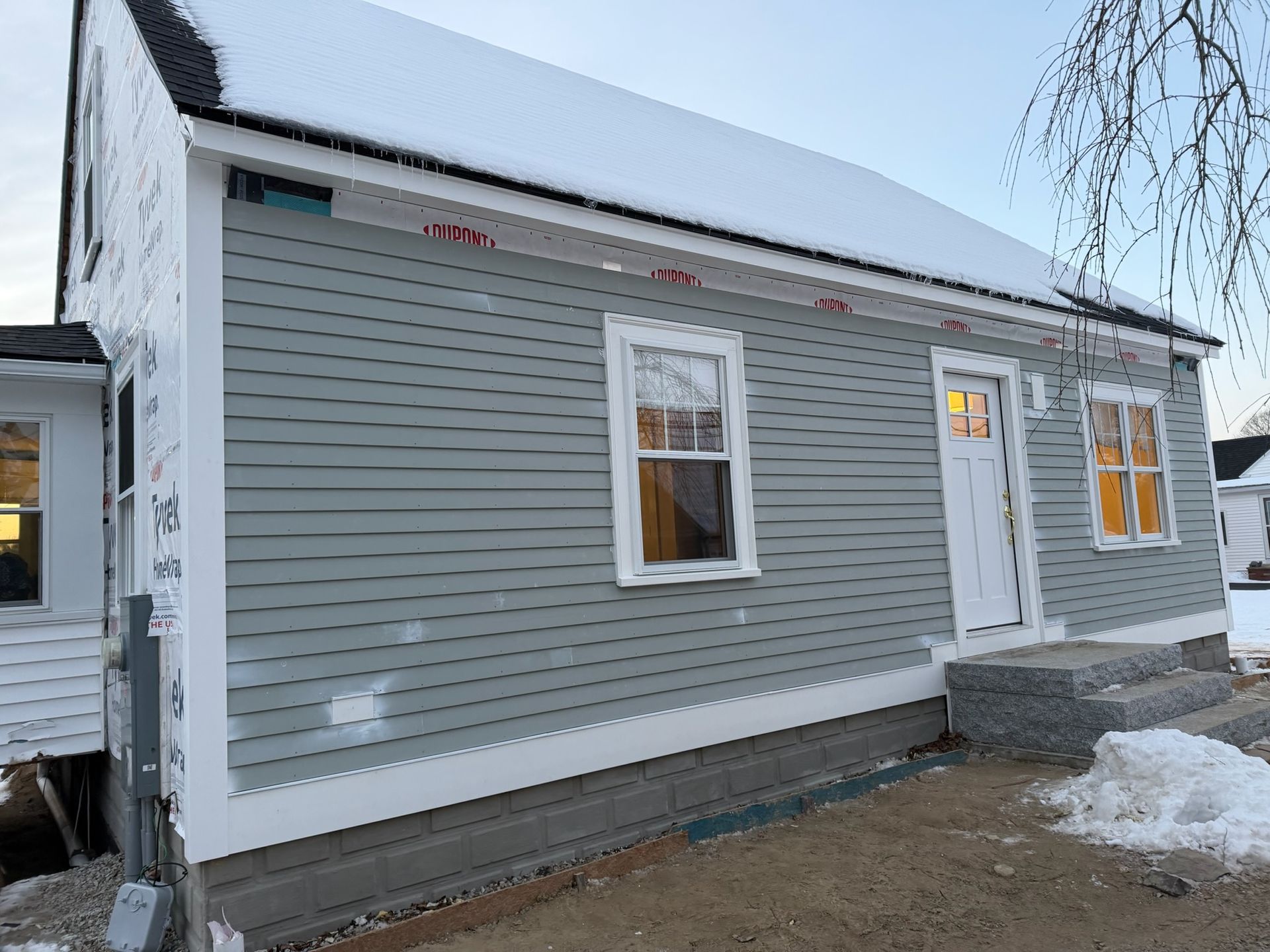 Gray siding on a house with a blue door, white trim, and a ladder against the side.