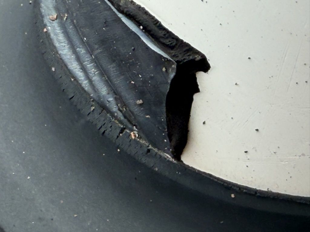 Close-up of a torn black rubber seal against a light gray surface