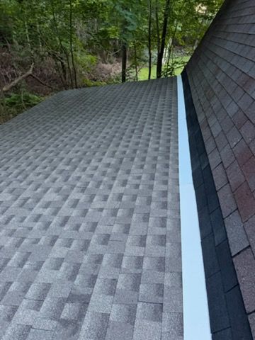 Gray shingle roof with a white gutter beside a wooded hillside