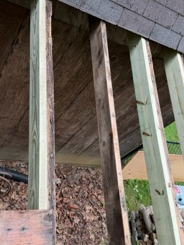 Under-deck framing with exposed wooden beams and joists next to a brick foundation.