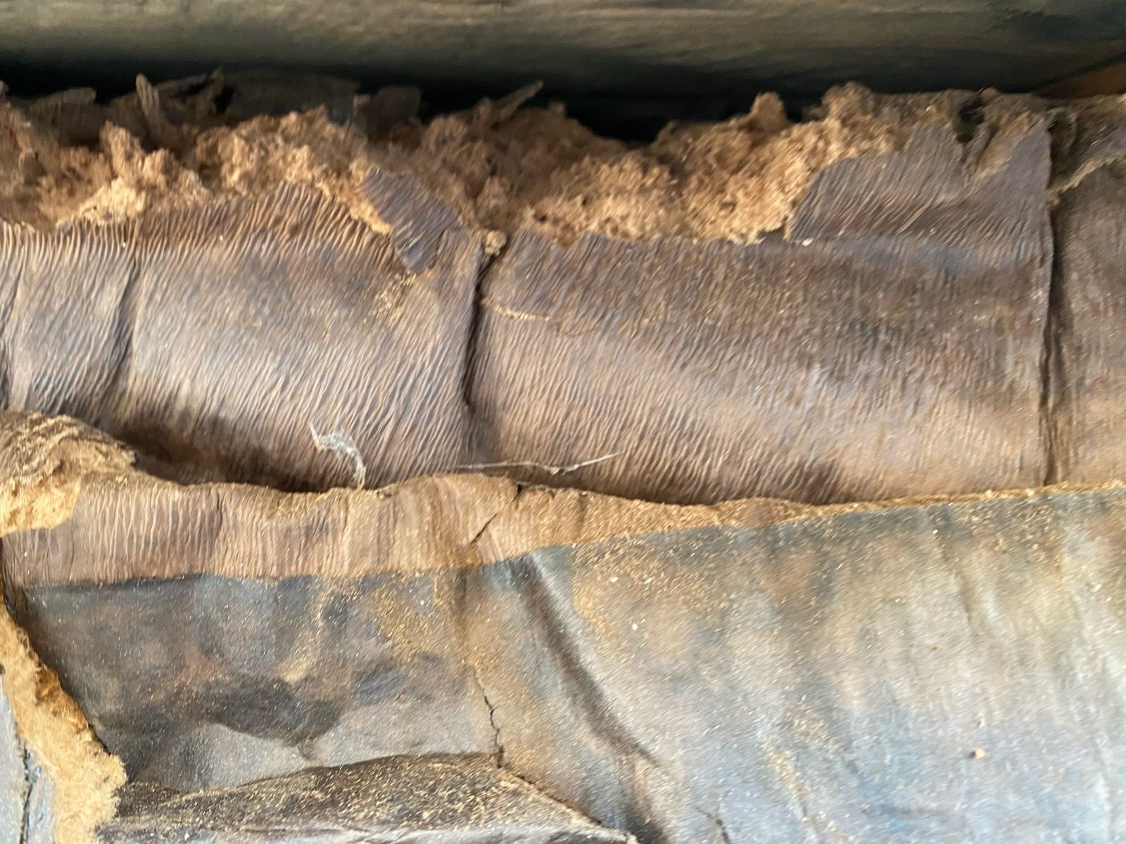 Close-up of a worn gray fabric seam with tan fraying edges and folded layers.