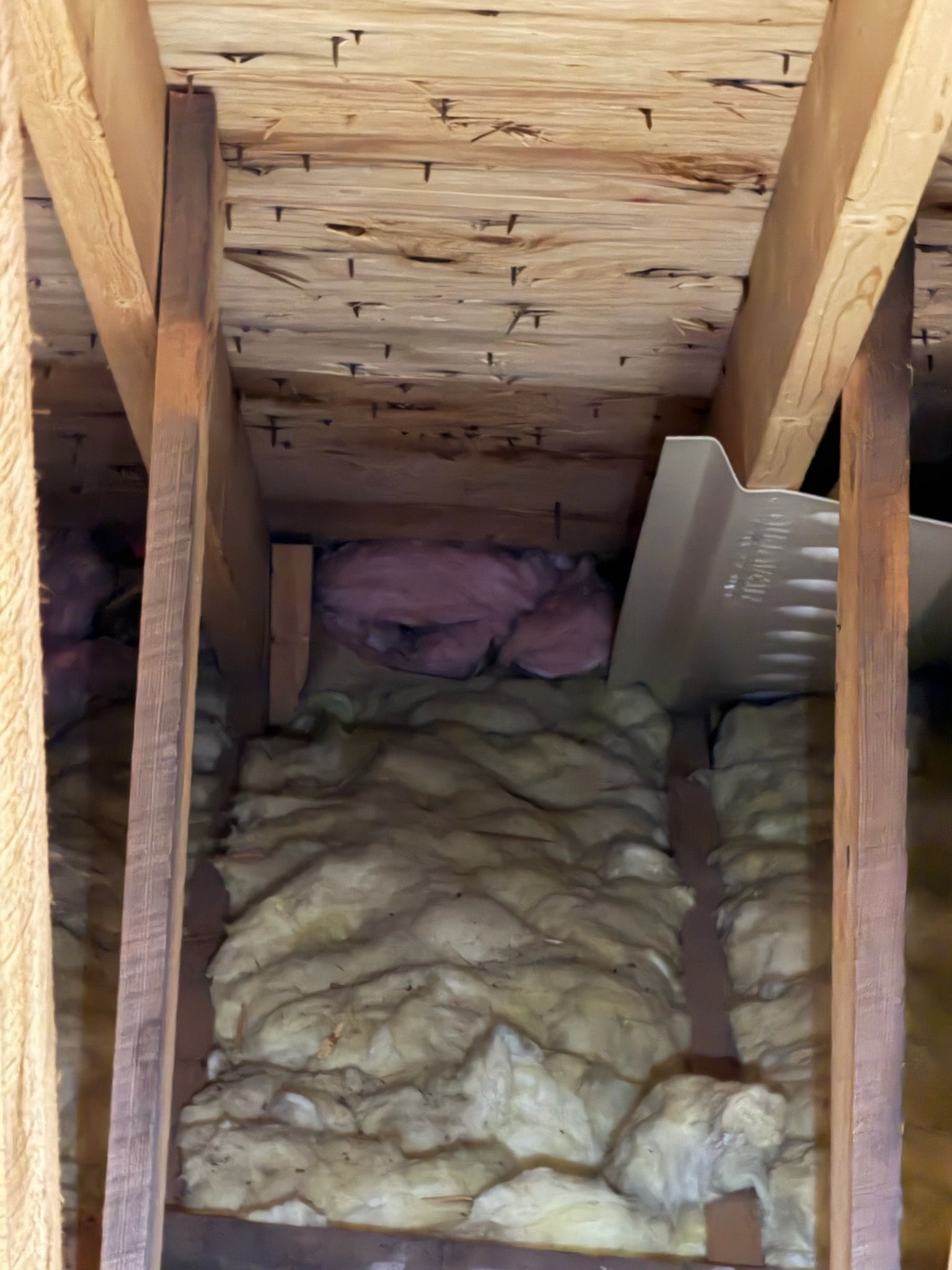 Attic crawlspace with exposed wood beams and yellow insulation batts on the floor and walls