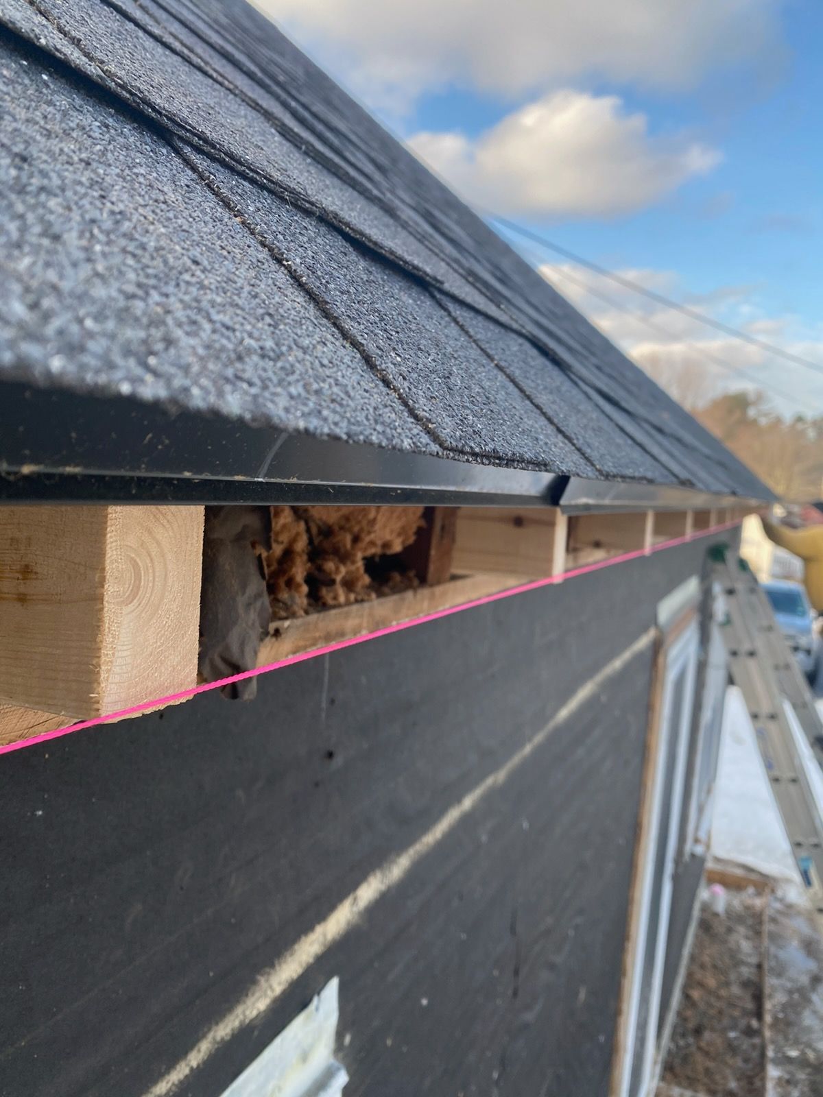Close-up of a roof edge with black shingles and exposed wood underlayment, under construction