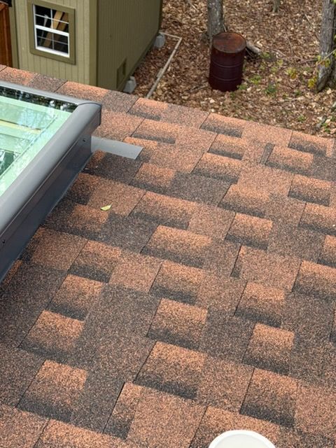 Rooftop shingles beside a skylight and downspout near a dormer wall with gravel below