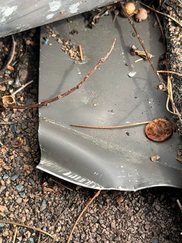 Cracked gray plastic panel on rocky ground with twigs and debris nearby