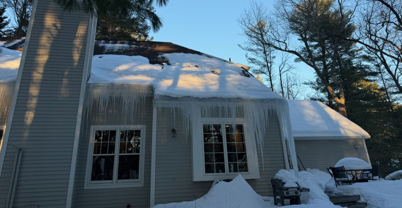Snow-covered house with icicles hanging from the roof in a wooded winter setting