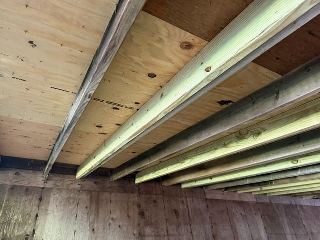 Wooden ceiling with exposed beams and plywood panels in an unfinished interior space