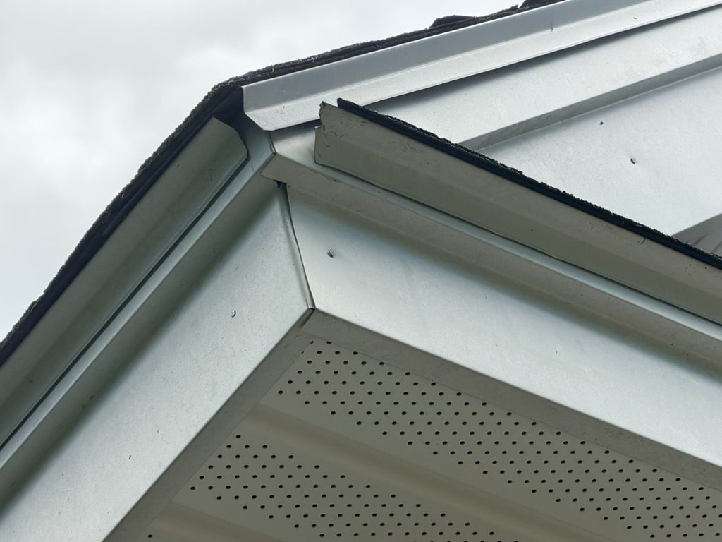 Close-up of a building roof corner with white siding, gray trim, and perforated soffit panels