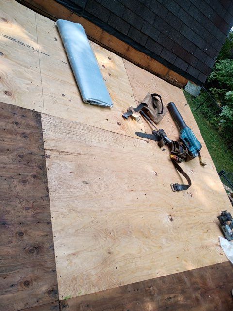 Tools and supplies laid out on plywood roof under repair, with blue insulation and a nail gun.