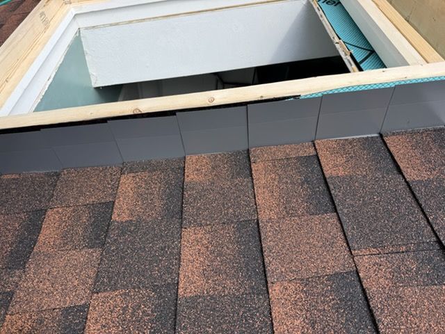 Open roof with exposed white fascia and brown shingles around a skylight opening