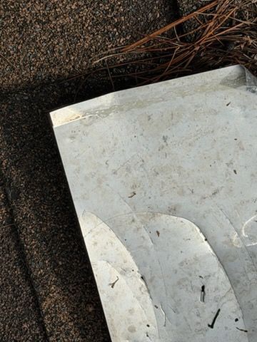 Close-up of a weathered white metal surface beside dark gravel and pine needles