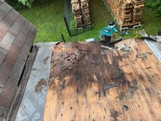 Damaged roof with blackened, weathered plywood and a worker inspecting near stacked materials