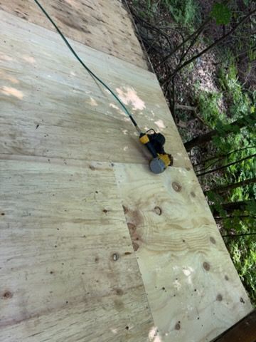 Person climbing a steep wooden wall with safety rope, outdoors near trees