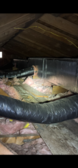 Attic insulation with exposed ductwork and wooden rafters, showing a dim crawlspace-like area.