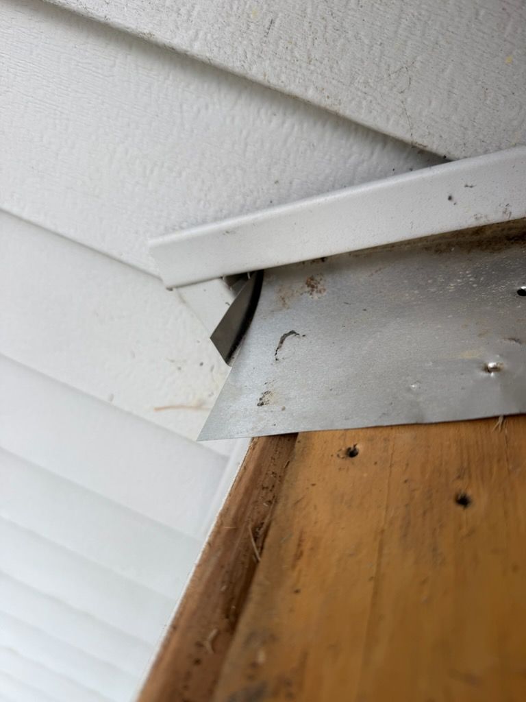 Damaged white siding and trim with a gap exposing the corner above a wooden surface