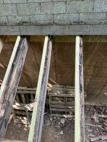 Damaged deck joists beneath a concrete ledge, showing exposed wood and rubble below.