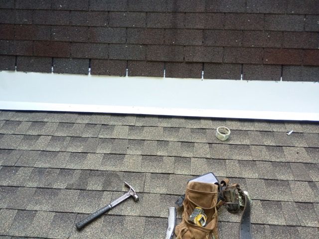 Roof with a hammer, bucket, and tools beside a roof vent and white flashing
