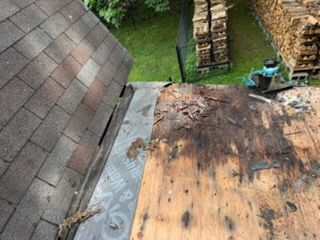 Roof deck with damaged wooden roofing and shingles near a chimney and stacked lumber outdoors