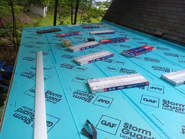 Blue roofing underlayment with scattered white boards and packaging on a sloped roof under construction