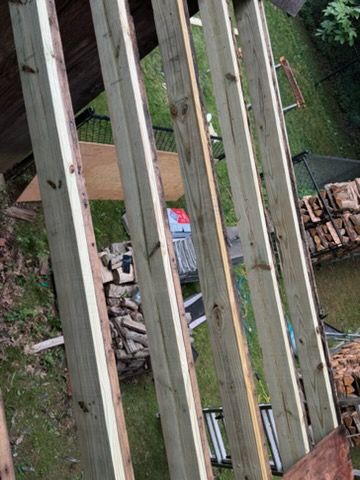 Looking down from a balcony onto a yard with stacked lumber, metal roofing, and a green lawn.