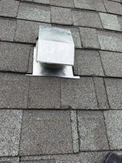 Roof vent protruding through gray asphalt shingles with a white flashing cover