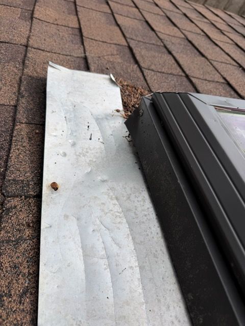 Damaged roof flashing beside a skylight, with debris and a bent metal strip on shingles