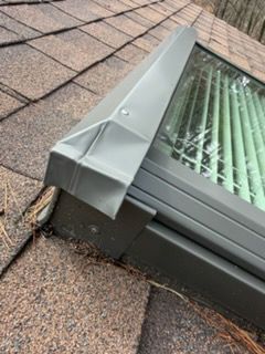 Damaged gray skylight flashing on a shingled roof, with bent metal at the corner.