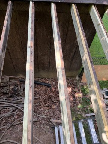 Weathered wooden deck boards over a cluttered ground area with leaves and a ladder below