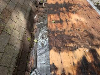 Rooftop with peeling orange wood, dark patches, and a narrow strip of metal flashing along the edge.