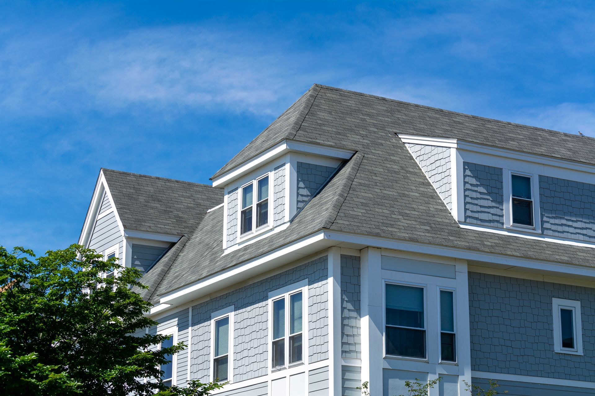 Blue house with gray shingled roof and white trim against a clear sky