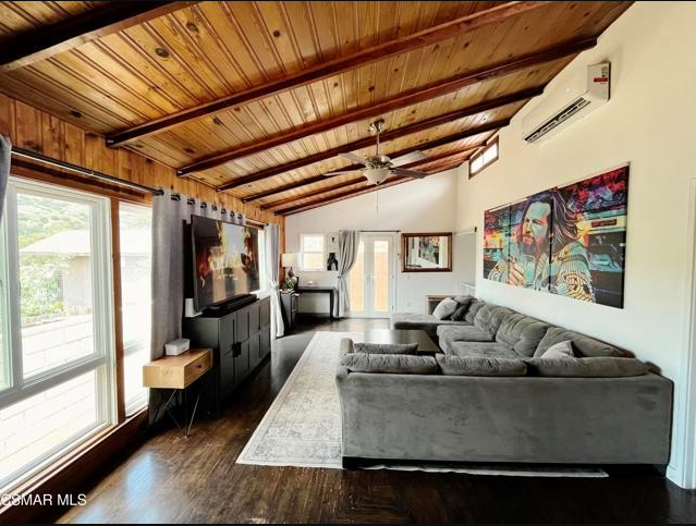 Living room with wooden ceiling, gray sectional sofa, art on wall, and large windows.