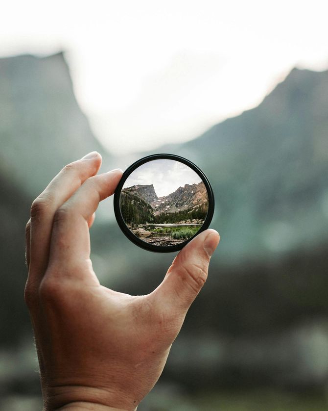 Hand holding a round lens, reflecting a mountain landscape.