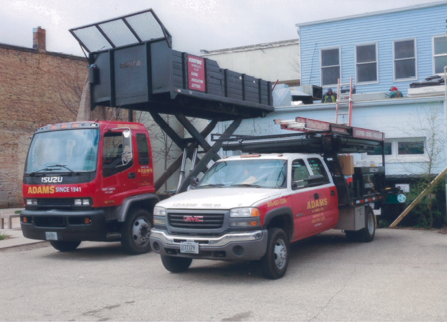 Two red and white trucks with a lift, parked near buildings.