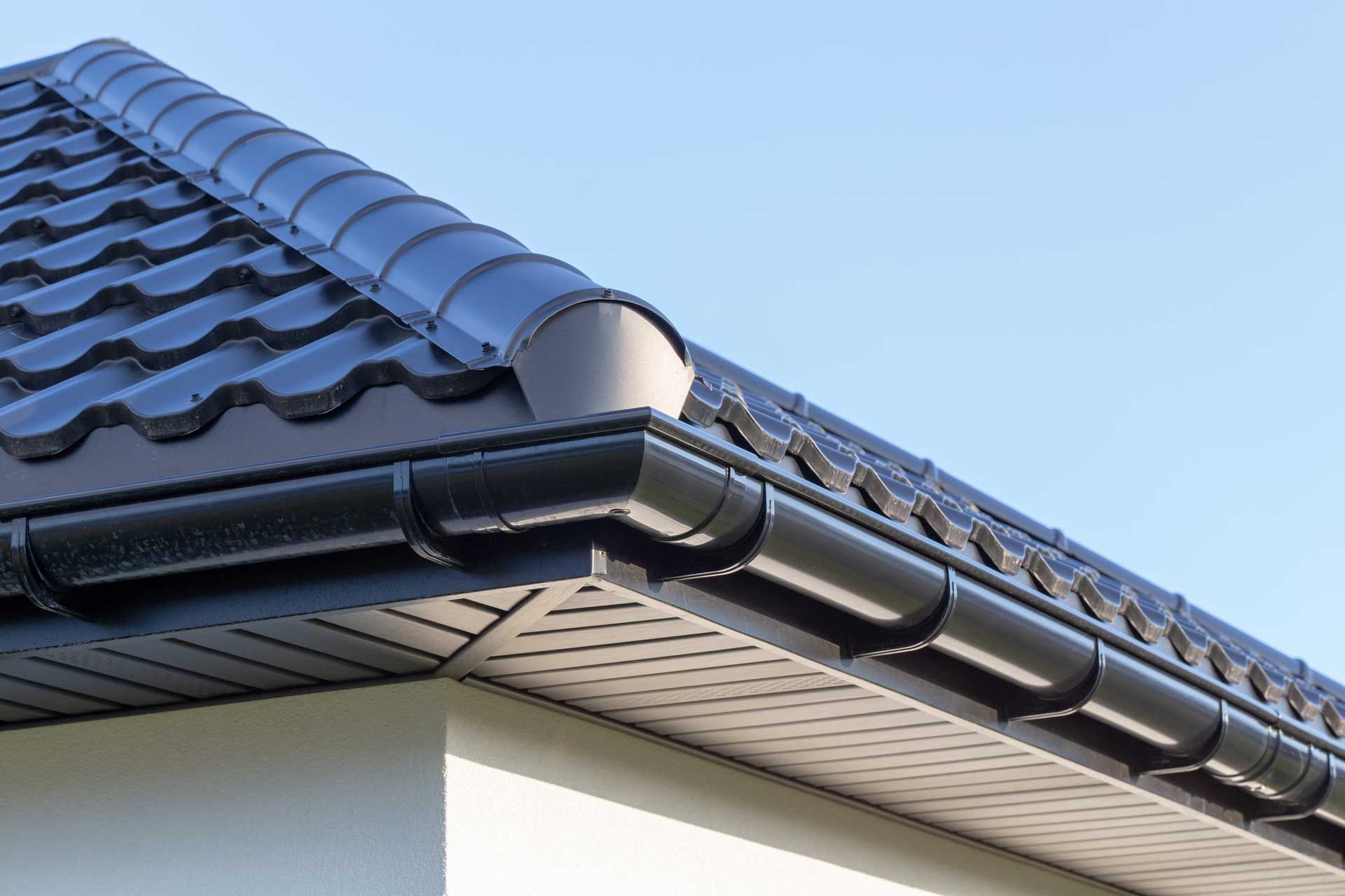 Black roof with matching gutters against a blue sky, close-up view. Black roof with matching gutters against a blue sky, close-up view.