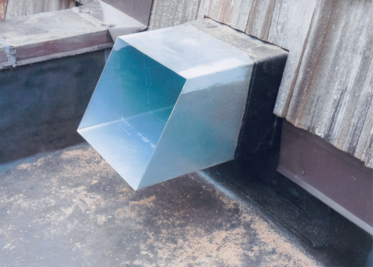 Metal chute extending from a dark roof, angled downwards, catching water.