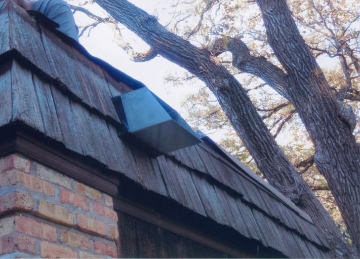 Man installing flashing on a wood shake roof near a large tree.