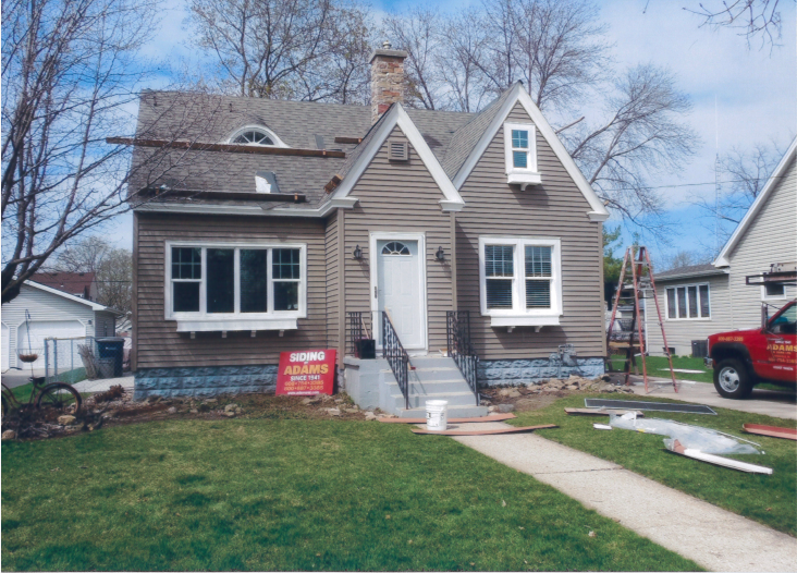 Brown house with new siding, white windows, and grey roof undergoing renovation; green lawn.
