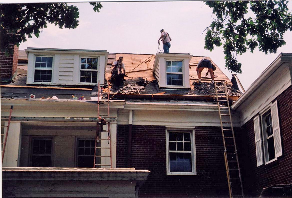 Dark gray roof corner with gutter, dark gray soffit, supported by a white wall and a dark column.