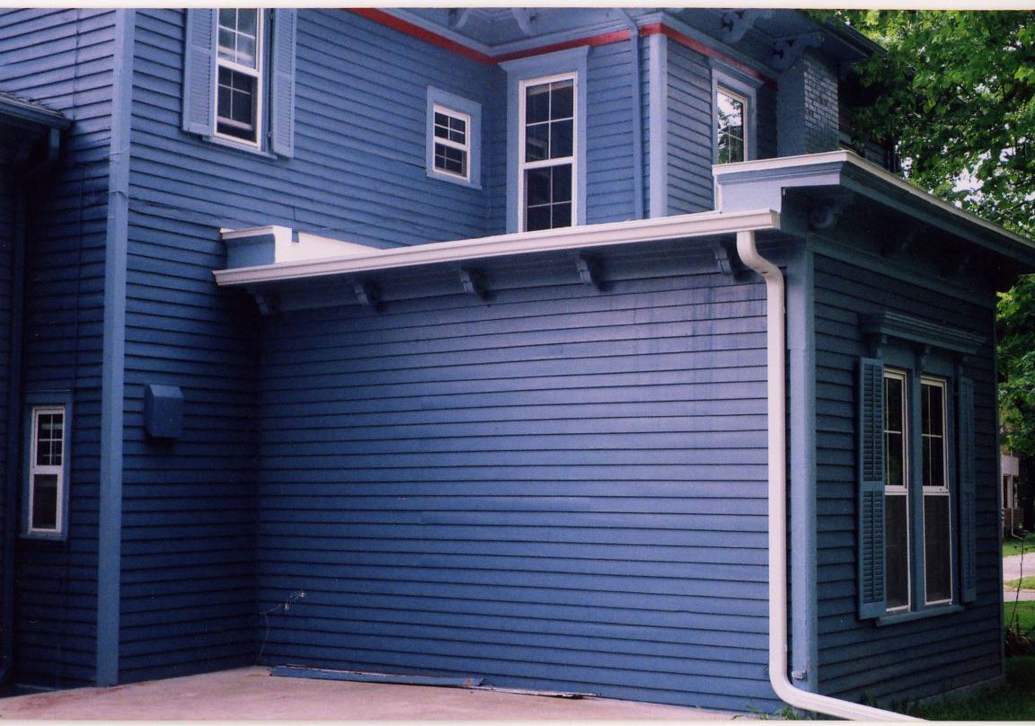 Gray building exterior with white gutters, a window, and a dark roof.