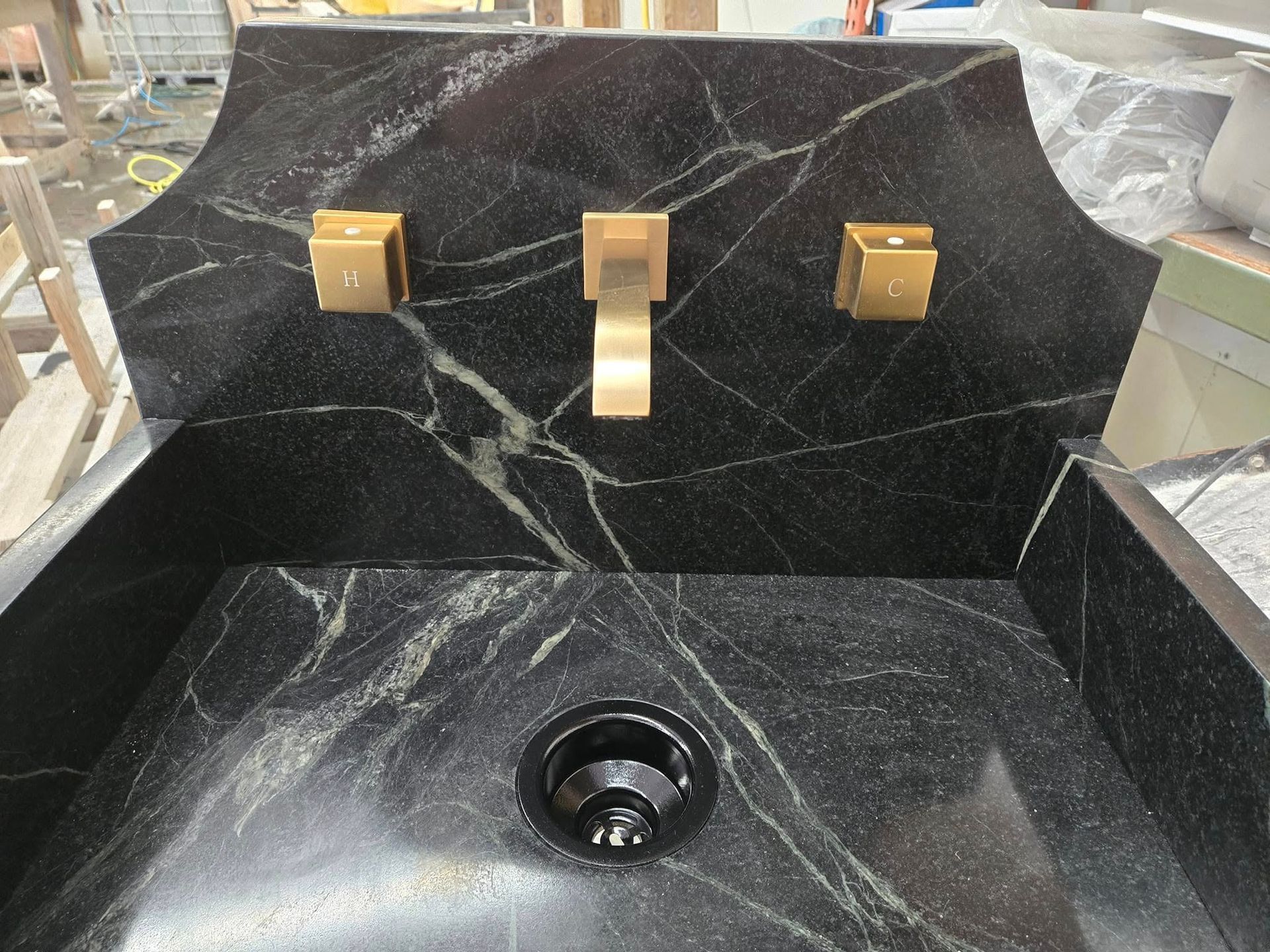 Black marble bathroom sink with gold faucets and a basin drain.