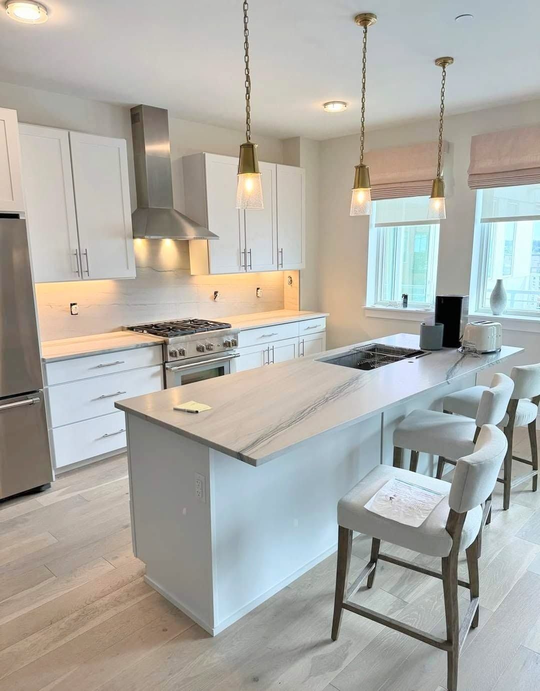 Bright modern white kitchen with island, pendant lights, and bar stools, seen from the dining area