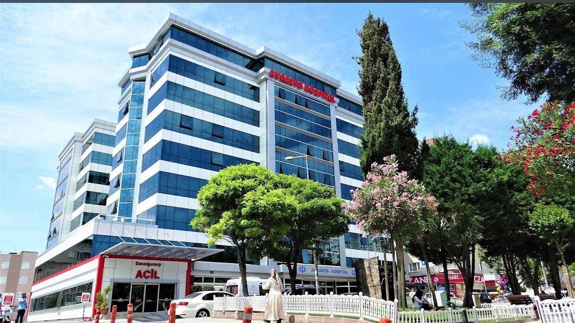 A multi-story office building with a blue glass facade and white accents, featuring an entrance with a red awning.