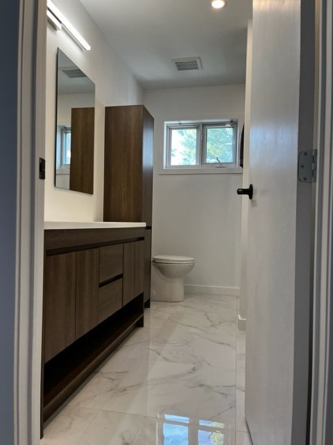 Salle de bain moderne avec lavabo en bois foncé, miroir, toilettes et sol en marbre blanc.