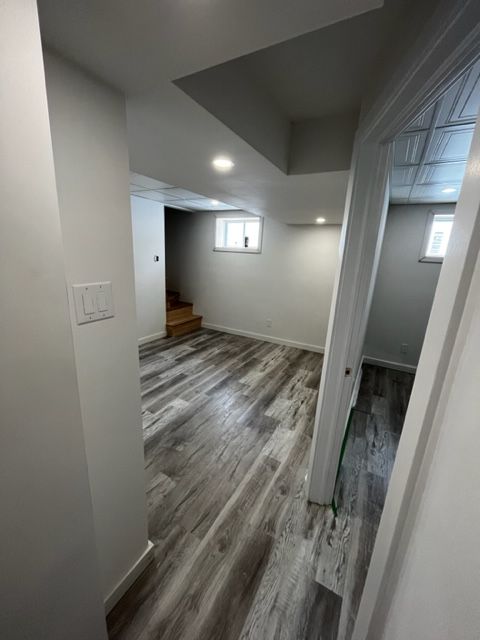Sous-sol rénové avec plancher gris, murs blancs, plafond abaissé et escalier en bois.